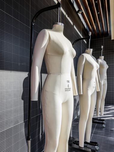 Dress forms on a rail against a dark tiled wall