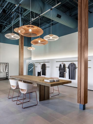 Copper pendant lights above a wood table and illuminated display wall